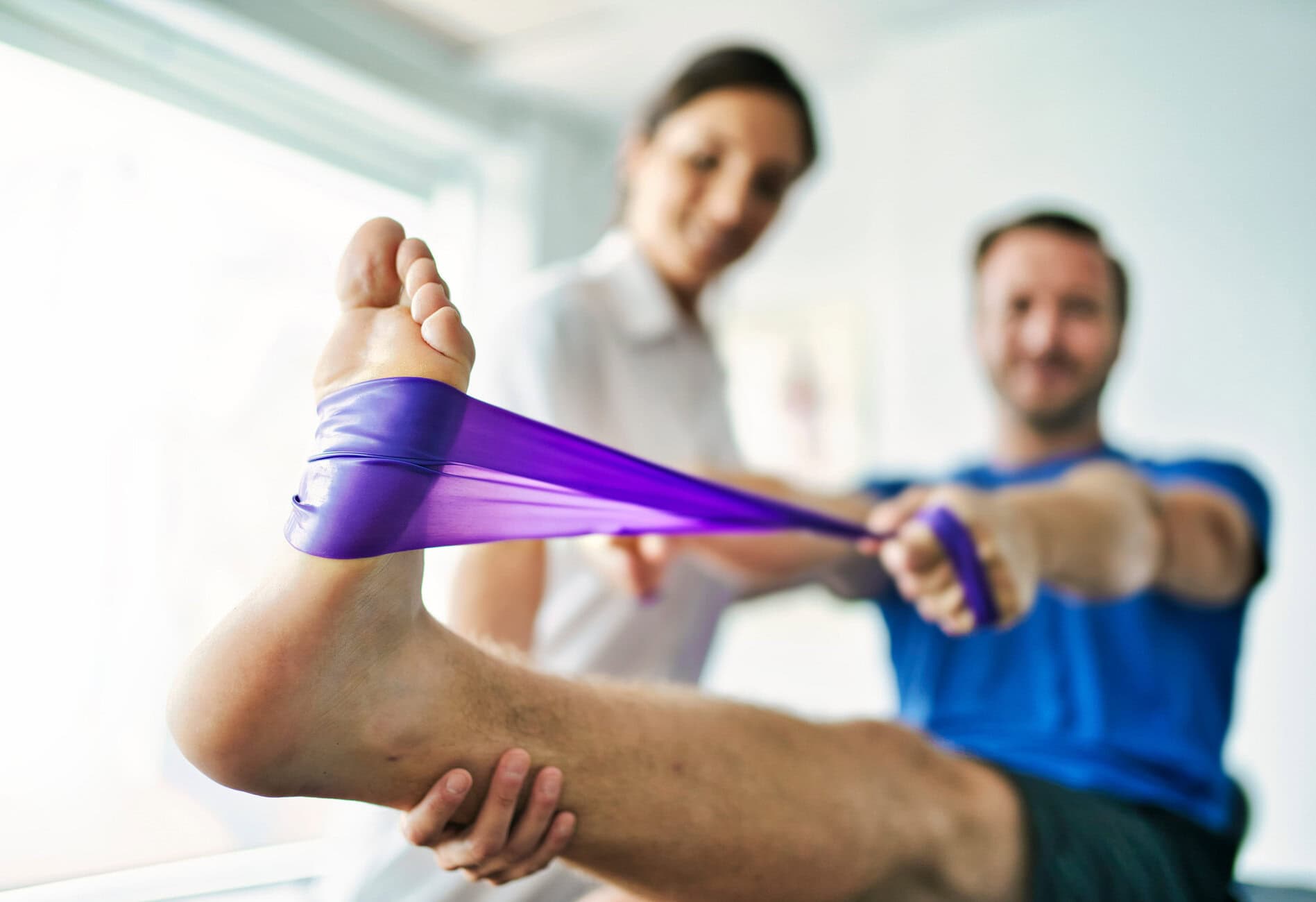 physiotherapist doing treatment with patient in bright office Physical therapists assist a client in a leg stretch using a purple resistance band during a physiotherapy session.