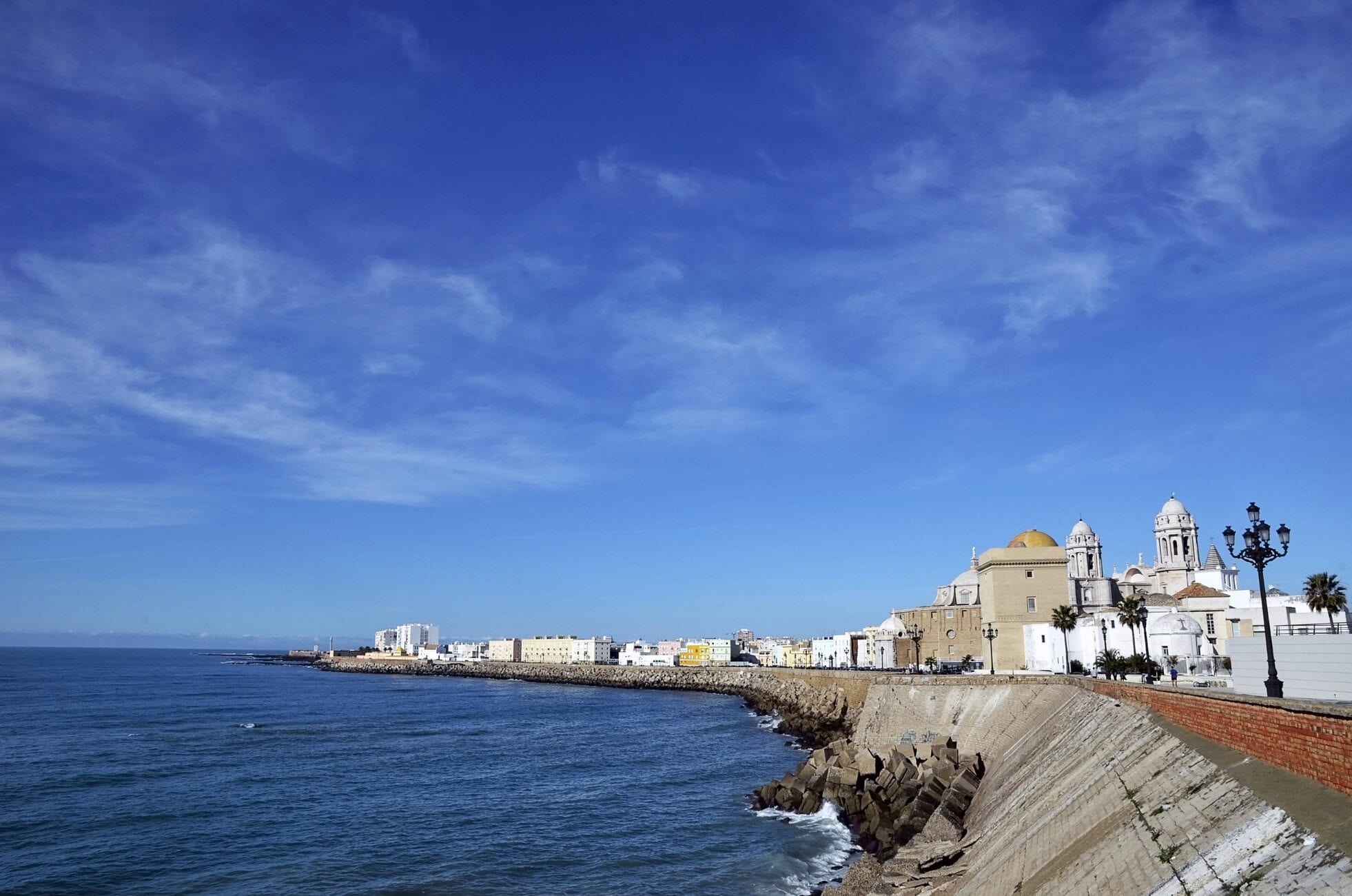CADIZ SPAIN Seaside cityscape with a stone breakwater, calm blue ocean, and white domed buildings along the shore.