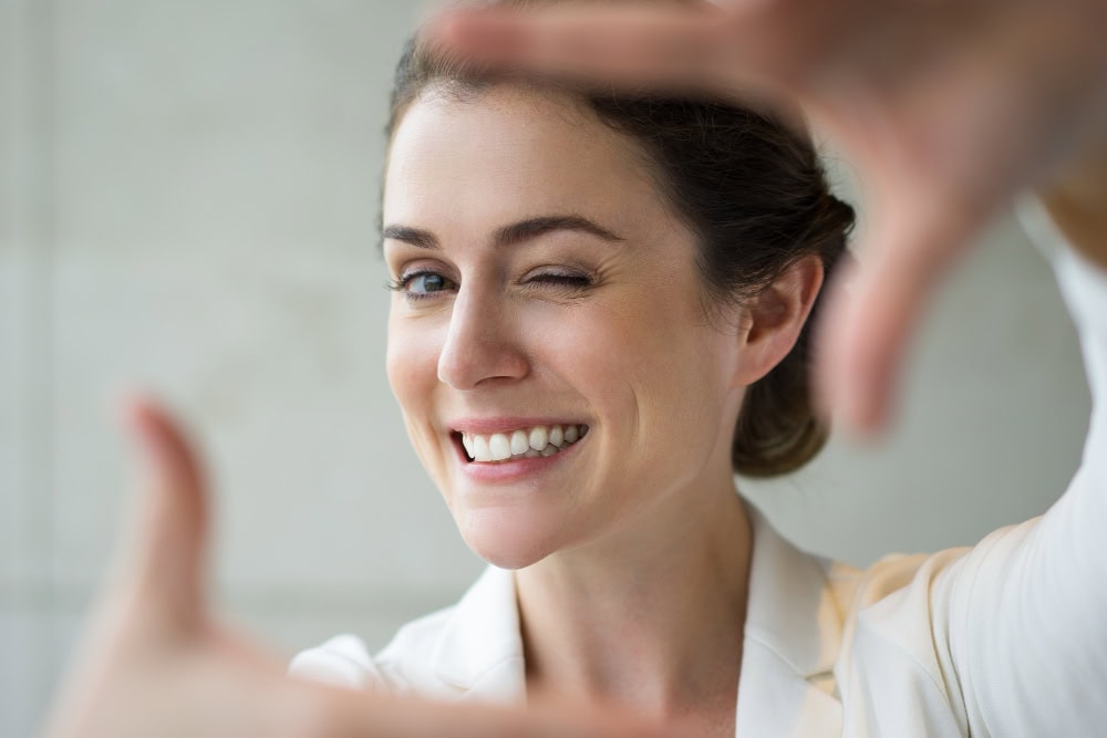 778206 – Clínica Dental Rident Smiling woman winking at the camera while taking a selfie, with hands framing the shot.