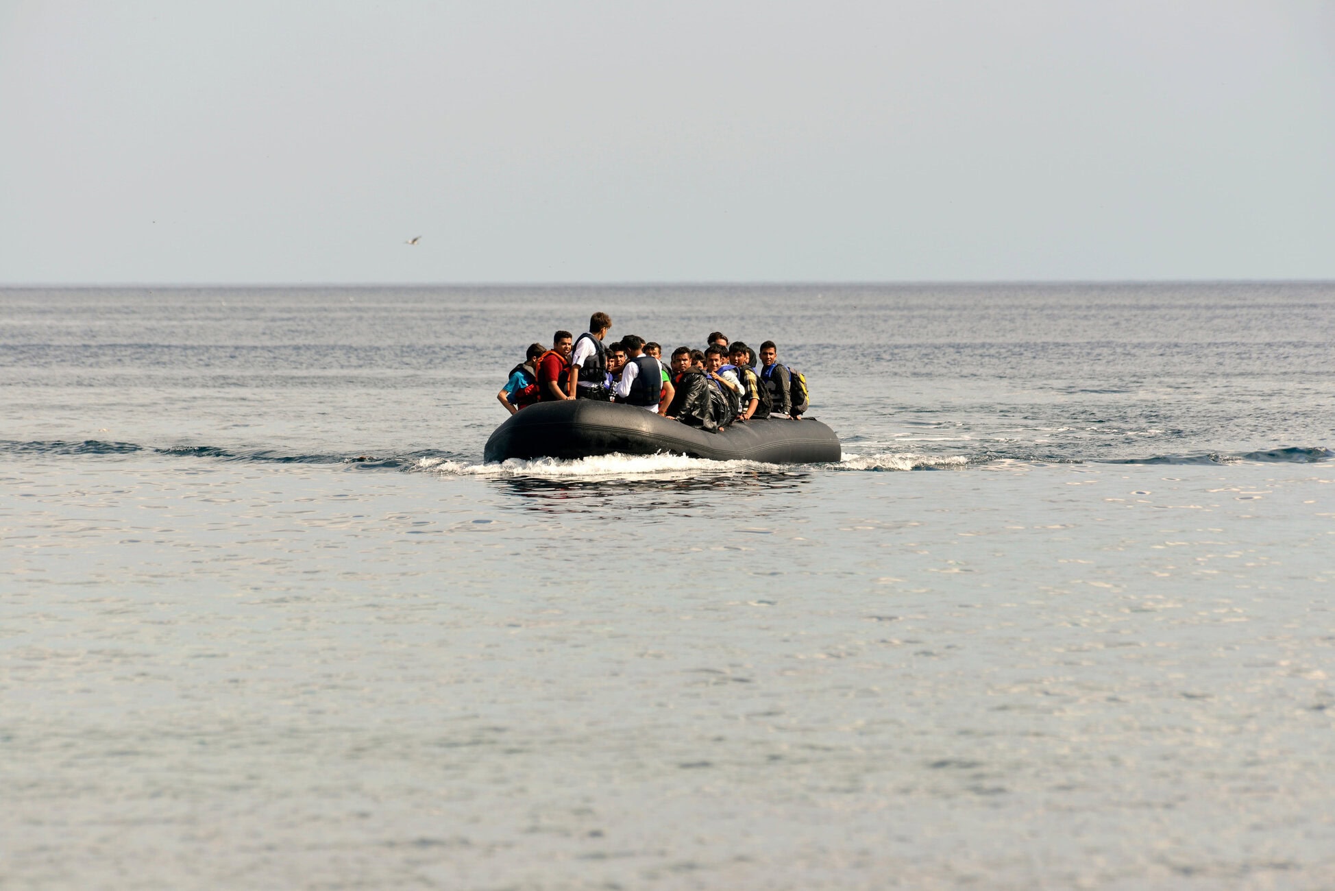 Politica migratoria UE – IP A group of people wearing life jackets crowded onto a black inflatable boat in the open sea, waves brushing the hull.