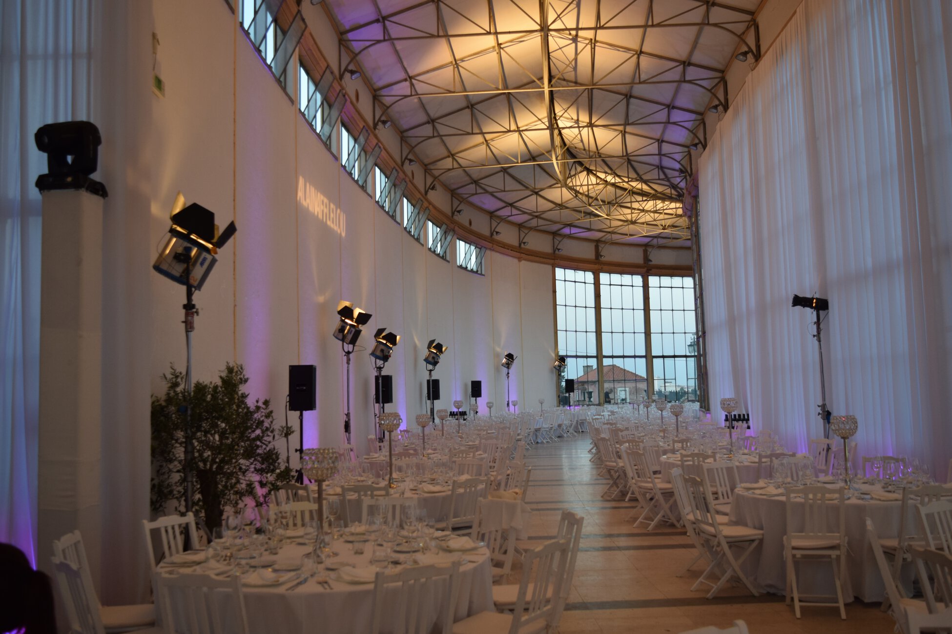 Detrás de cada evento exitoso existe un equipo de planificación especializado – 779448 – Elite Conexión Indoor banquet hall set for a formal event with round tables, white chairs, glassware, and purple uplighting.