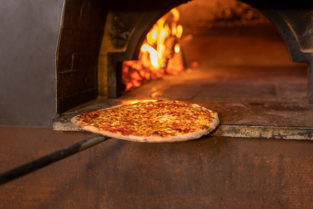 Pizza being slid into a hot wood-fired oven for baking.